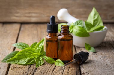 Fesleğen yağı ve taze yapraklar ahşap masada, yakın plan.