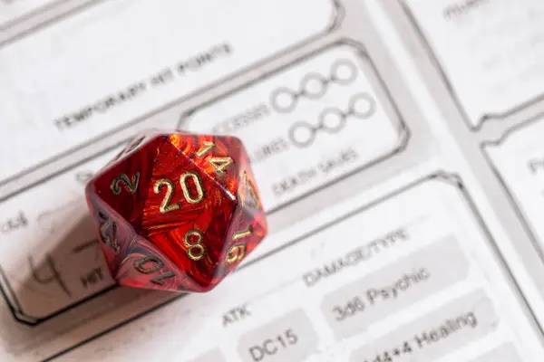 Kırmızı bir D20 'ye odaklanın. Detaylı bir rol yapma oyunu karakter kağıdına güvenerek ölün. Oyun stratejisini ve şansını sembolize edin.