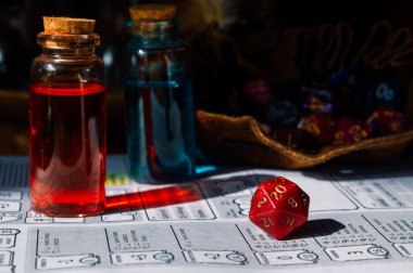 Canlı kırmızı bir D20 die, iksir şişeleri ve masa başı rol yapma oyunu için hazırlanmış bir karakter listesi..