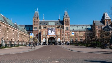 Amsterdam, Hollanda - 20 Mart 2025 Kargo motosikletli bisikletçi Amerikan Fotoğraf Sergisi bayrağı altında Rijksmuseum 'dan geçiyor