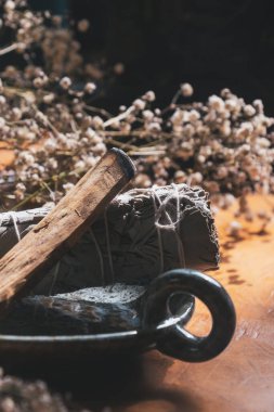 Kurumuş çiçeklerle çevrili seramik tabakta Palo Santo ve adaçayı lekesi