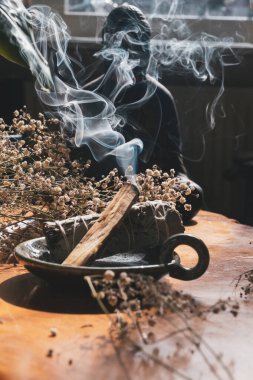 Yanan adaçayı ve Palo Santo, ahşap masada kurumuş çiçeklerle çevrili körling dumanına yapışırlar.