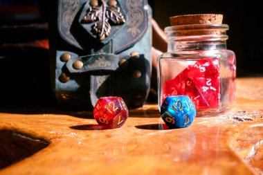 Kırmızı ve mavi bir D12 ölür tahta bir yüzey üzerinde bir zar kavanozu ve dekoratif bir deri kesenin yanında dinlenir..