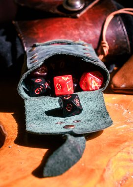 Deri bir kese, masa başı rol yapma oyunları için mükemmel olan ahşap bir masaya renkli çokyüzlü zarlar döker..