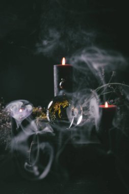 Siyah mumlar ve dönen dumanlarla çevrili kristal küre karanlık bir ayin alanında gizemli ve büyülü bir atmosferi çağrıştırıyor.