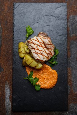 Kızarmış biberli domuz pirzolası ve siyah bir taş üzerinde patates, dikey.