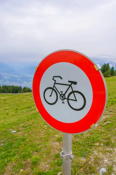 Traffic sign forbidden to pass bicycles, black bicycle silhouette with white background and outer red circle, on a wooden pole in a natural landscape with trees background. Symbol, signal, direction