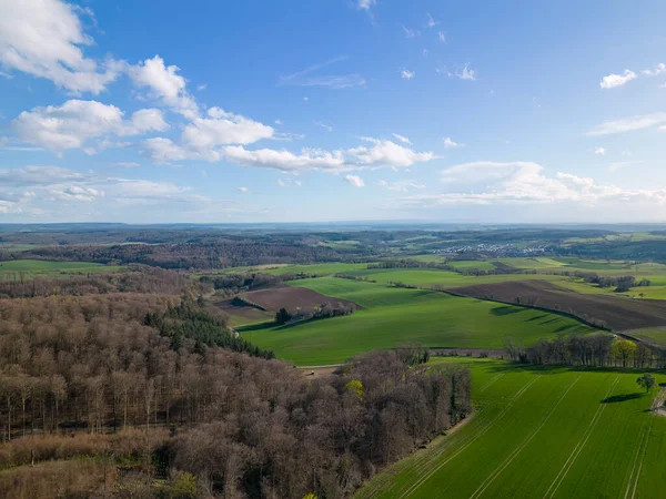 Drone View over Kraichgau in Germany in spring. Forest and field with blue cloudy sky.