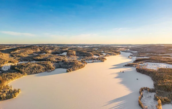 Aerial view of a gold sunset over winter snow-covered forest. Aerial drone view of a winter landscape. Beautiful sunset sky over frozen lake.