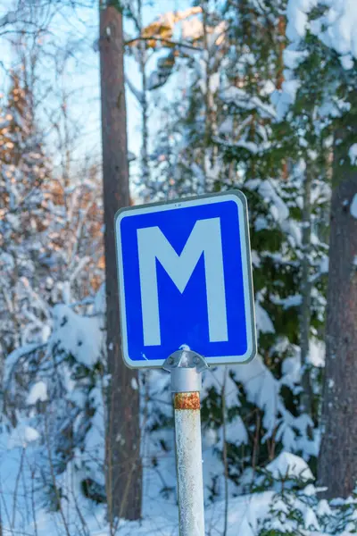 Roadsign M meeting point in winter forest