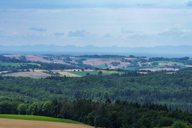 Dramatik bir gökyüzü altında, geniş tarlaları ve bulutları olan üzüm bağlarıyla çevrili bir köy güzel bir manzara yaratır.