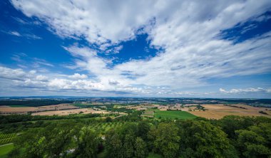 Dramatik bir gökyüzü altında, geniş tarlaları ve bulutları olan üzüm bağlarıyla çevrili bir köy güzel bir manzara yaratır.