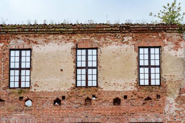 Kırık camları olan terk edilmiş, eski bir tuğla bina. Duvarlar yıpranmış ve yaşlanmış işaretler gösteriyor.