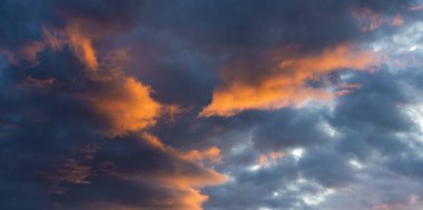 Gökyüzünün dinamik bulutlarla dolu büyüleyici bir görüntüsü ve sıcak bir günbatımının canlı renkleri güzelliği gösteriyor.