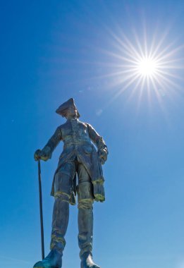Cesur bir askerin çarpıcı ve güçlü heykeli parlak mavi gökyüzüne ve parlak güneşe karşı dimdik ayakta duruyor.