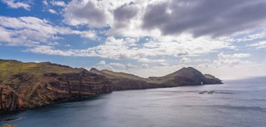 Ponta de Sao Lourencos 'un Atlantik Okyanusu' yla buluşan engebeli uçurumlarının nefes kesici manzarası. Dağınık bulutlu açık gökyüzü Madeira 'ya dokunulmamış kıyı güzelliği, doğa ve seyahat temaları için ideal.
