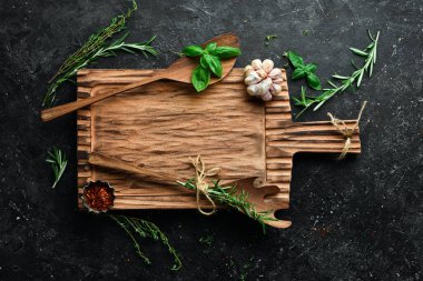 Ev yapımı yemek tariflerinin afişi. Mutfak eski ahşap tahta, baharatlar ve otlar, yazı için boş yer. Siyah taştan bir arka planda. Üst görünüm.