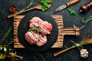 Domuz pirzolasına sarılmış domuz pirzolası, siyah bir tabakta biberiye ve kekik ile servis edilir. Siyah taştan bir arka planda. Üst görünüm.