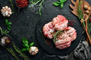 Domuz pirzolasına sarılmış domuz pirzolası, siyah bir tabakta biberiye ve kekik ile servis edilir. Siyah taştan bir arka planda. Üst görünüm.