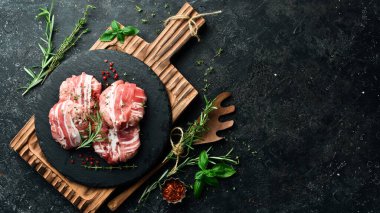 Domuz pirzolasına sarılmış domuz pirzolası, siyah bir tabakta biberiye ve kekik ile servis edilir. Siyah taştan bir arka planda. Üst görünüm.