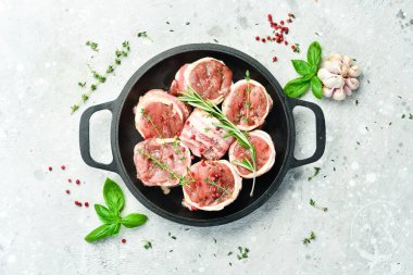 Pastırmaya sarılmış domuz filetosu. Tavada, pişirmeye hazır. Beton bir arka planda. Üst görünüm.