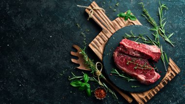 Çiğ, sulu biftek. Biberiyeli ve baharatlı mayalanmış biftek pişirmeye hazır. - Et. Siyah taştan bir arka planda. Üst görünüm.