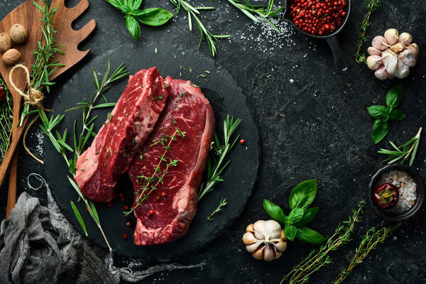 Raw juicy striploin steak. Fermented steak with rosemary and spices is ready for cooking. Meat. On a black stone background. Top view.