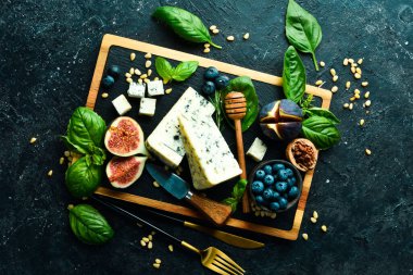 Tahtada dilimlenmiş peynir. Mavi peynir, incir, yabanmersini ve bal. Beton bir arka planda. Üst görünüm.