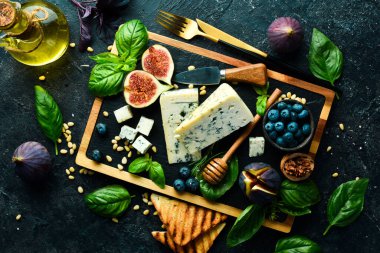 Tahtada dilimlenmiş peynir. Mavi peynir, incir, yabanmersini ve bal. Beton bir arka planda. Üst görünüm.