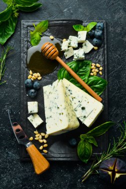 Siyah taş tabakta küflü mavi peynir fesleğen ve bal. Siyah taştan bir arka planda. Üst görünüm.