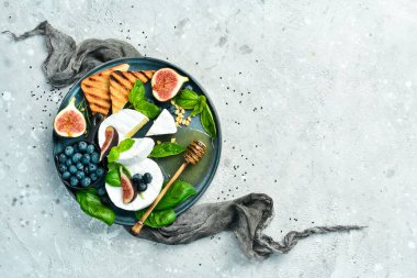 Brie peyniri, bal ve mavi tabakta incir. Beton bir arka planda. Üst görünüm.