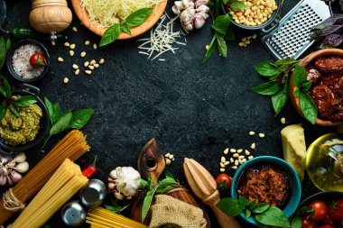 Aşçılık geçmişi: makarna, fesleğen, parmesan, pesto, domates ve fındık, zeytinyağı. Siyah taş arka planda.