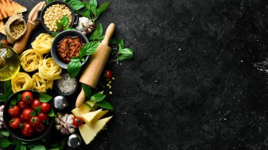 İtalyan mutfağı geçmişi: makarna, fesleğen, parmesan, pesto, domates ve fındık, zeytinyağı. Siyah taş arka planda.