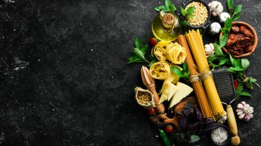 İtalyan mutfağı geçmişi: makarna, fesleğen, parmesan, pesto, domates ve fındık, zeytinyağı. Siyah taş arka planda.