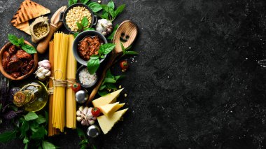 Pesto soslu spagetti ve kurutulmuş domates pişiriyorum. İçindekiler: spagetti, fesleğen, parmesan, çam fıstığı, domates, baharat. İtalyan geleneksel mutfağı. Beton bir arka planda.