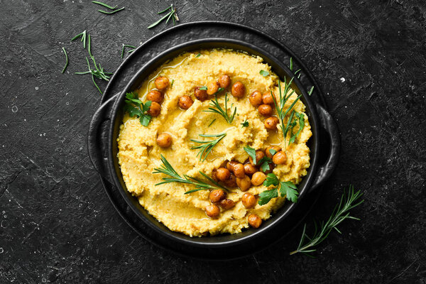 Hummus with chickpeas and rosemary in a black stone plate. Vegetarian food. Top view. On a black stone background.