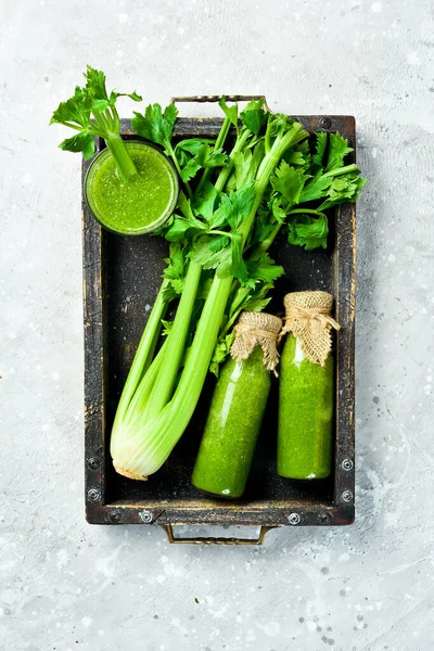 A bottle of celery juice in a box on a stone background. Vegetarian drink. A stalk of fresh celery. Free space for text.
