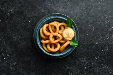 Aperatif. Sos ve tuzlu kızarmış soğan halkaları. Siyah taştan bir arka planda.