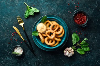 Aperatif. Sos ve tuzlu kızarmış soğan halkaları. Siyah taştan bir arka planda.