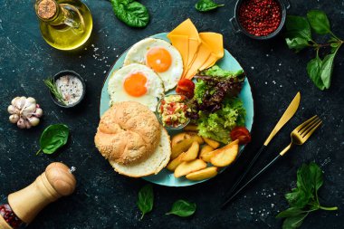 Kahvaltıda. Çırpılmış yumurta, çörek, peynir, salata ve sos. Siyah taştan bir arka planda.