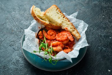 Deniz ürünleri. Domates sosunda pişirilmiş karides ve midye, kızarmış ekmekle servis edilir. Siyah taştan bir arka planda.