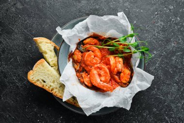 Deniz ürünleri. Domates sosunda pişirilmiş karides ve midye, kızarmış ekmekle servis edilir. Siyah taştan bir arka planda.