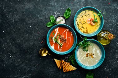 Renkli çorba seti. Domates çorbası, balkabağı ve mantar çorbası. Mavi bir tabakta. Siyah taştan bir arka planda.