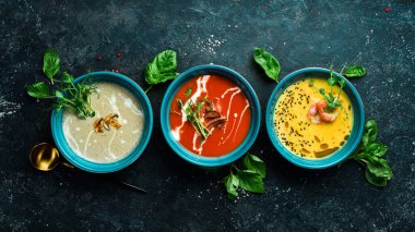 Renkli çorba seti. Domates çorbası, balkabağı ve mantar çorbası. Mavi bir tabakta. Siyah taştan bir arka planda.