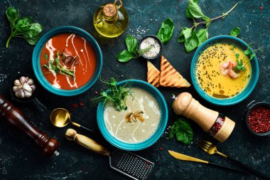 Renkli çorba seti. Domates çorbası, balkabağı ve mantar çorbası. Mavi bir tabakta. Siyah taştan bir arka planda.