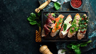 Ton balıklı, peynirli, jambonlu ve domatesli sandviç seti. Siyah taştan bir arka planda.