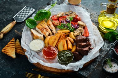 Barbekü. Ahşap bir tahtanın üzerinde ızgara sebzeli ızgara dana biftek ve tavuk göğsü. Siyah taştan bir arka planda.