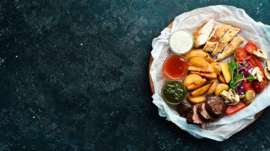 Barbekü. Ahşap bir tahtanın üzerinde ızgara sebzeli ızgara dana biftek ve tavuk göğsü. Siyah taştan bir arka planda.