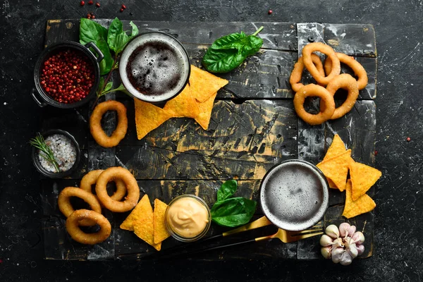 Salty snacks for beer: grilled onion rings and nachos. On a black stone background.