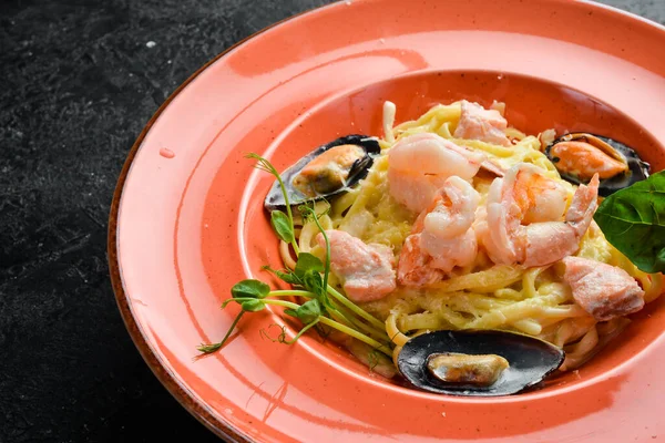 Seafood. Pasta with shrimp, mussels, cheese and basil in a plate. Italian dish. On a black stone background.